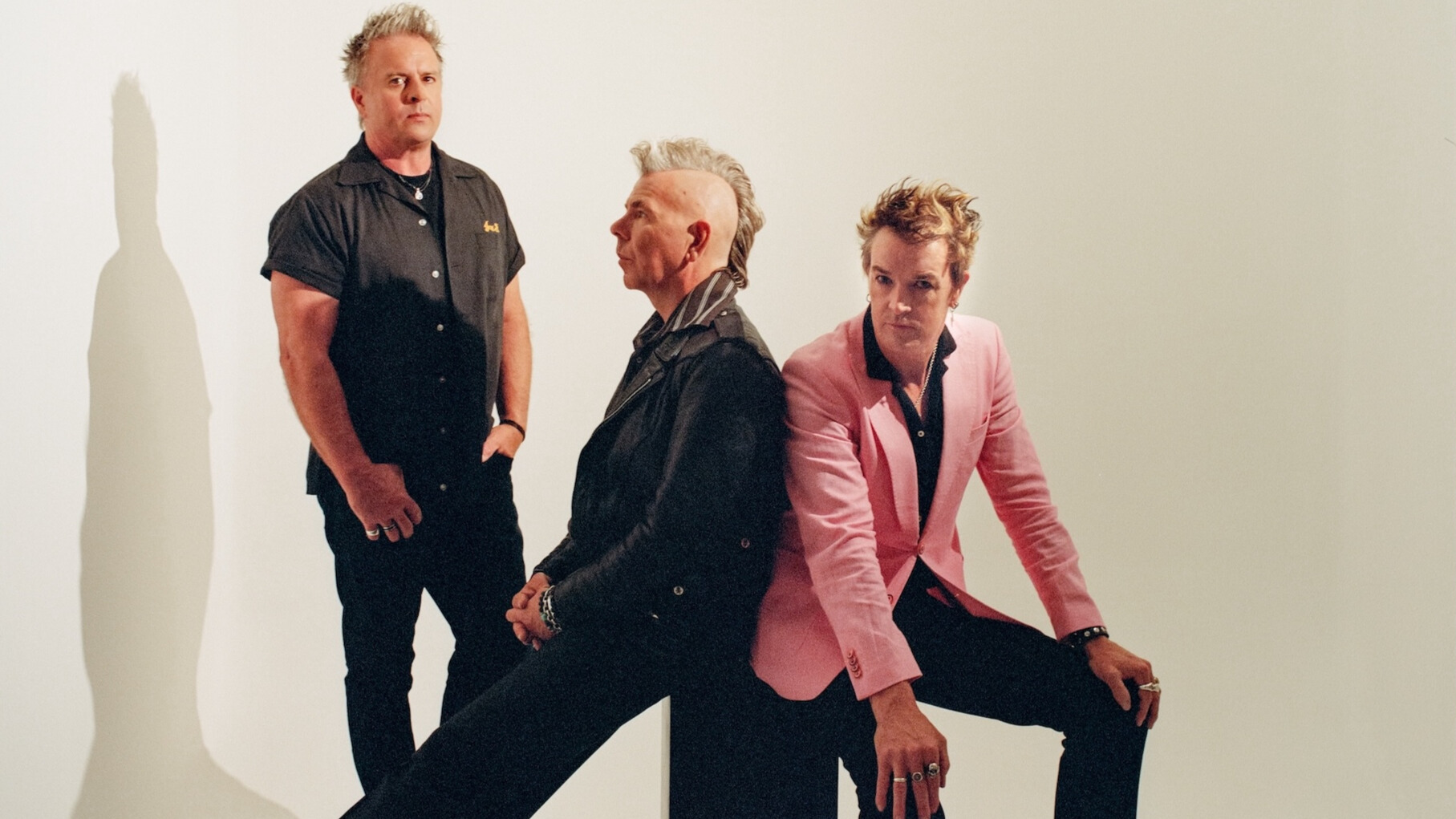 Punk three-piece The Living End sitting and standing in a shadowy white room