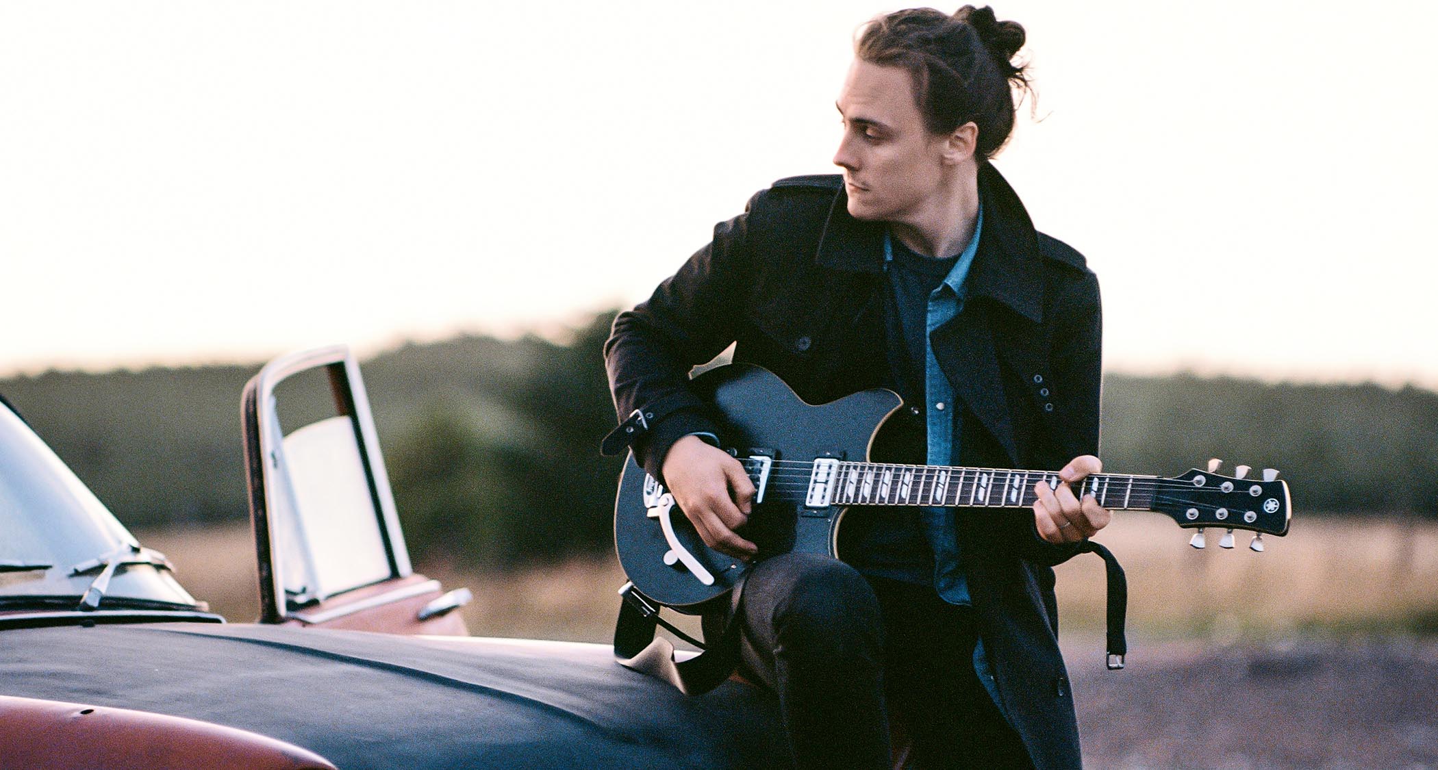 Chris Buck sitting on the hood of car, playing a Yamaha Revstar