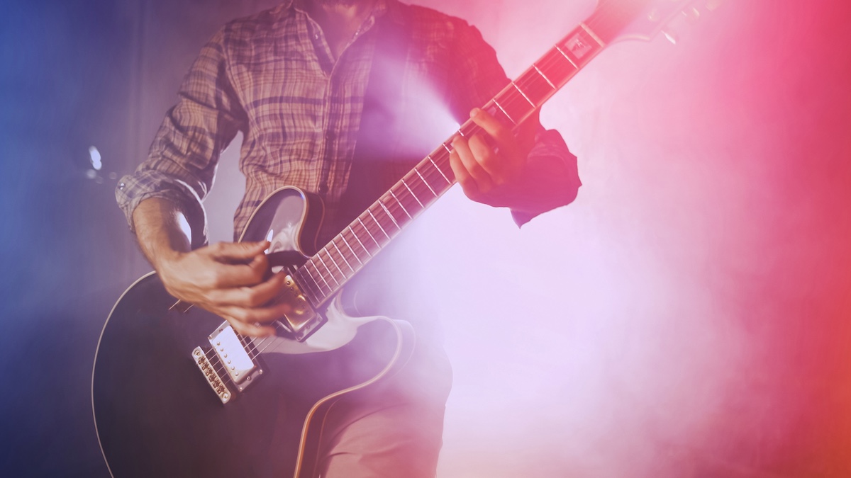 Man plays guitar on stage surrounded by dry ice and blue and pink light